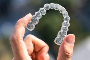 A hand holding an Invisalign clear aligner tray.